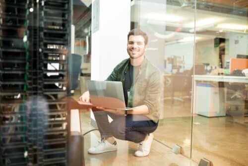 portrait-happy-young-male-network-engineer-with-laptop-hand-working-datacenter-1-scaled-500x335